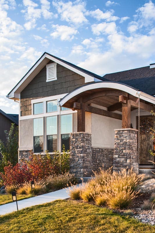 House plan exterior with stone base, arched wooden porch entrance, stone pillars, and stacked gables with decorative vent.