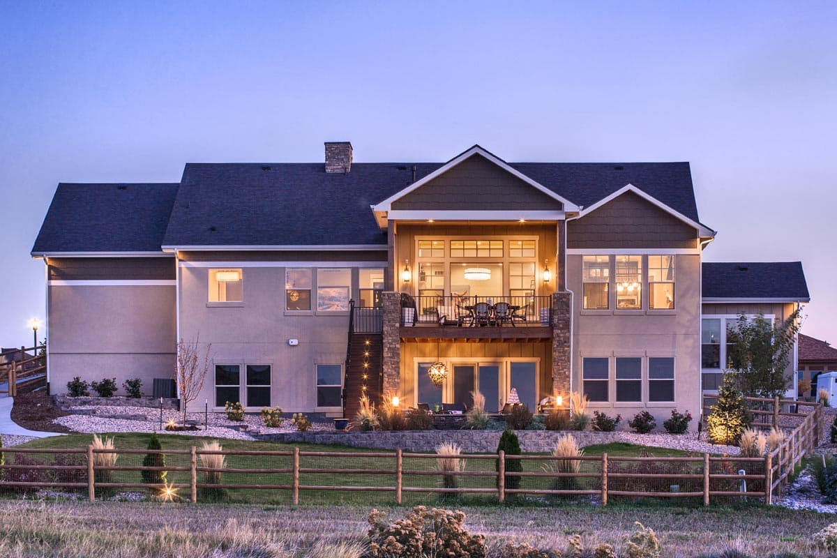 House plan exterior: Two-story Modern Farmhouse with layered gables, upper balcony with railing, and stone-clad columns.