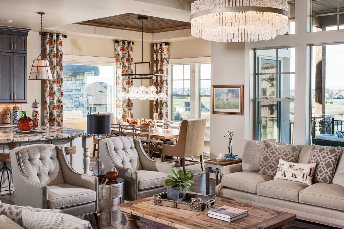 Open-concept living and dining space with tufted armchairs, sectional sofa, large windows, and a wood-paneled ceiling.