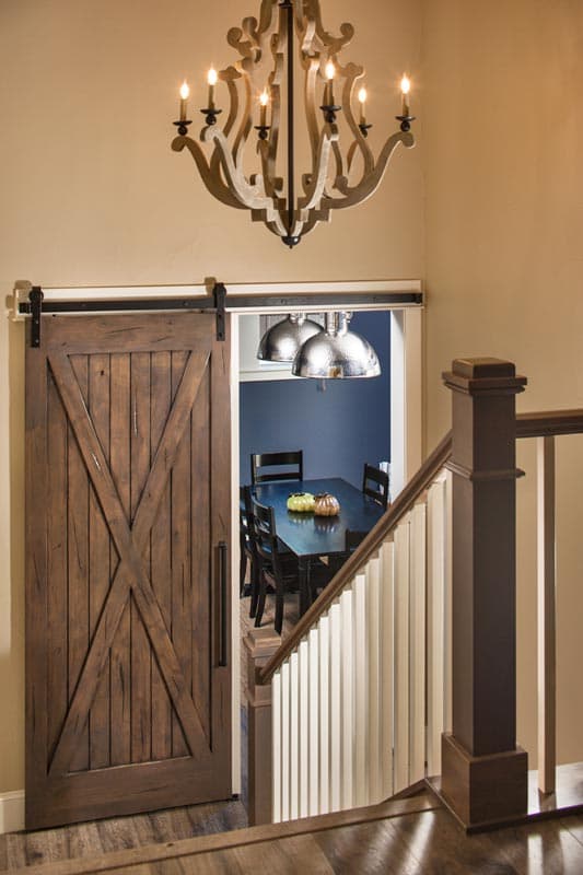 Interior view showing a rustic wooden barn door opening to a dining room with a dark table and chairs.