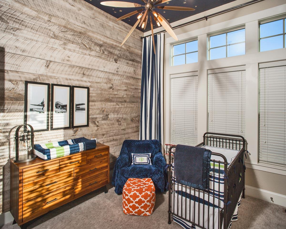 Nursery with wood-plank walls, a crib, dresser, armchair, and large windows.