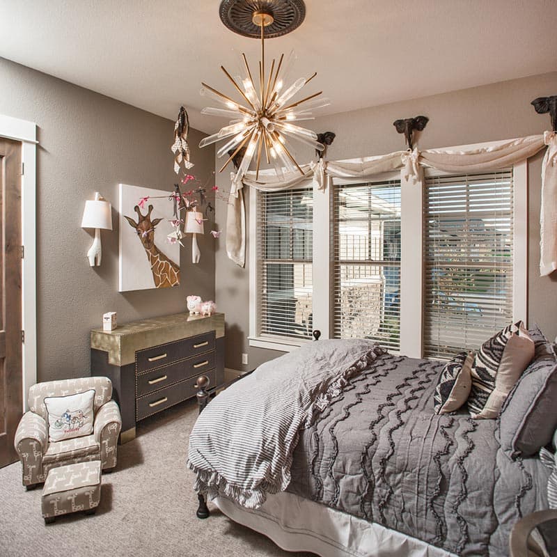 Child's bedroom with giraffe artwork, dresser, small armchair and ottoman, and a bed with striped bedding.