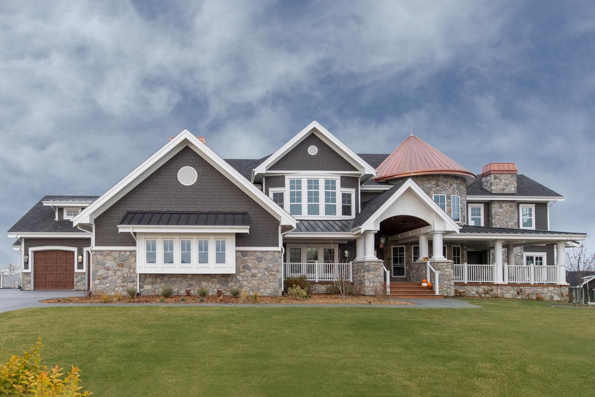 House plan exterior: Two-story home with stone and shingle siding, prominent gables, bay window, and a circular turret with copper roof.