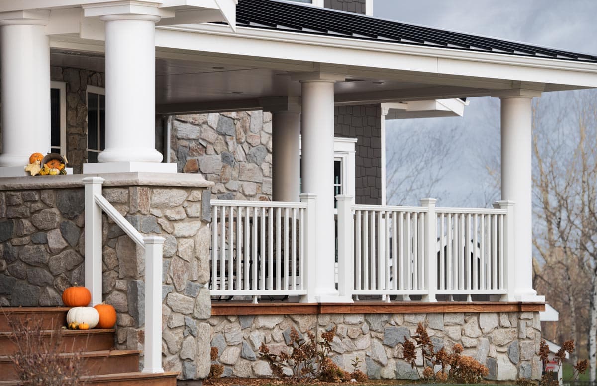House plan exterior with stone facade, covered porch, white balustrade, and Doric columns.