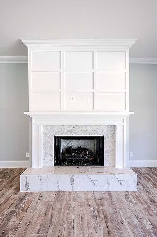 Interior view of a fireplace with marble tile surround, wood-burning insert, and paneled wall above.