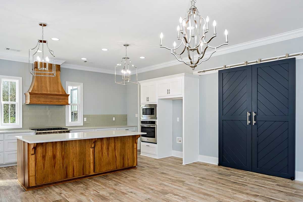 Interior view of a kitchen featuring a large wooden island, built-in ovens, and dark blue chevron barn doors.