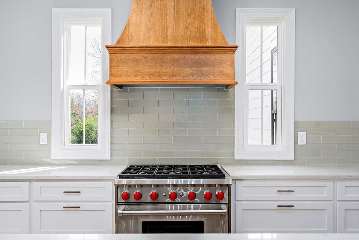 Kitchen featuring a stainless steel range, wood range hood, subway tile backsplash, and double-hung windows.