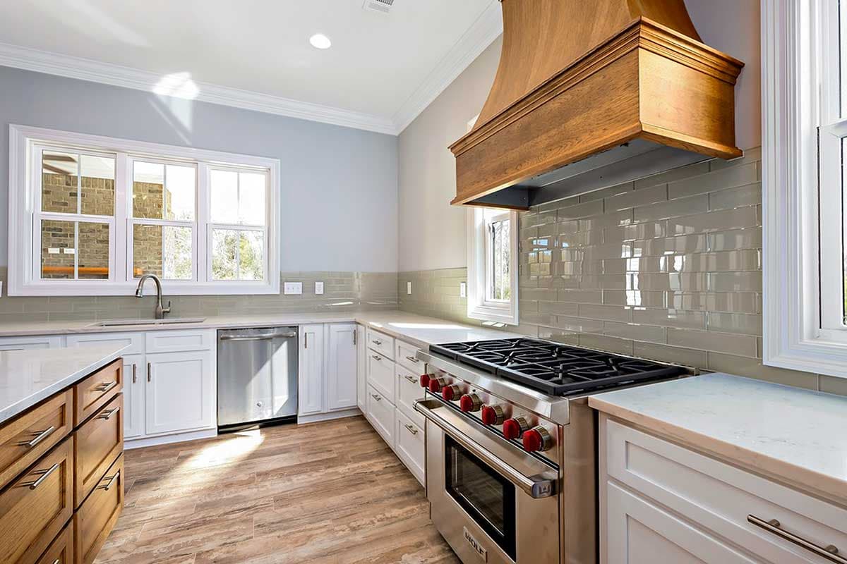Kitchen with stainless steel range, wooden hood, white cabinetry, and subway tile backsplash.