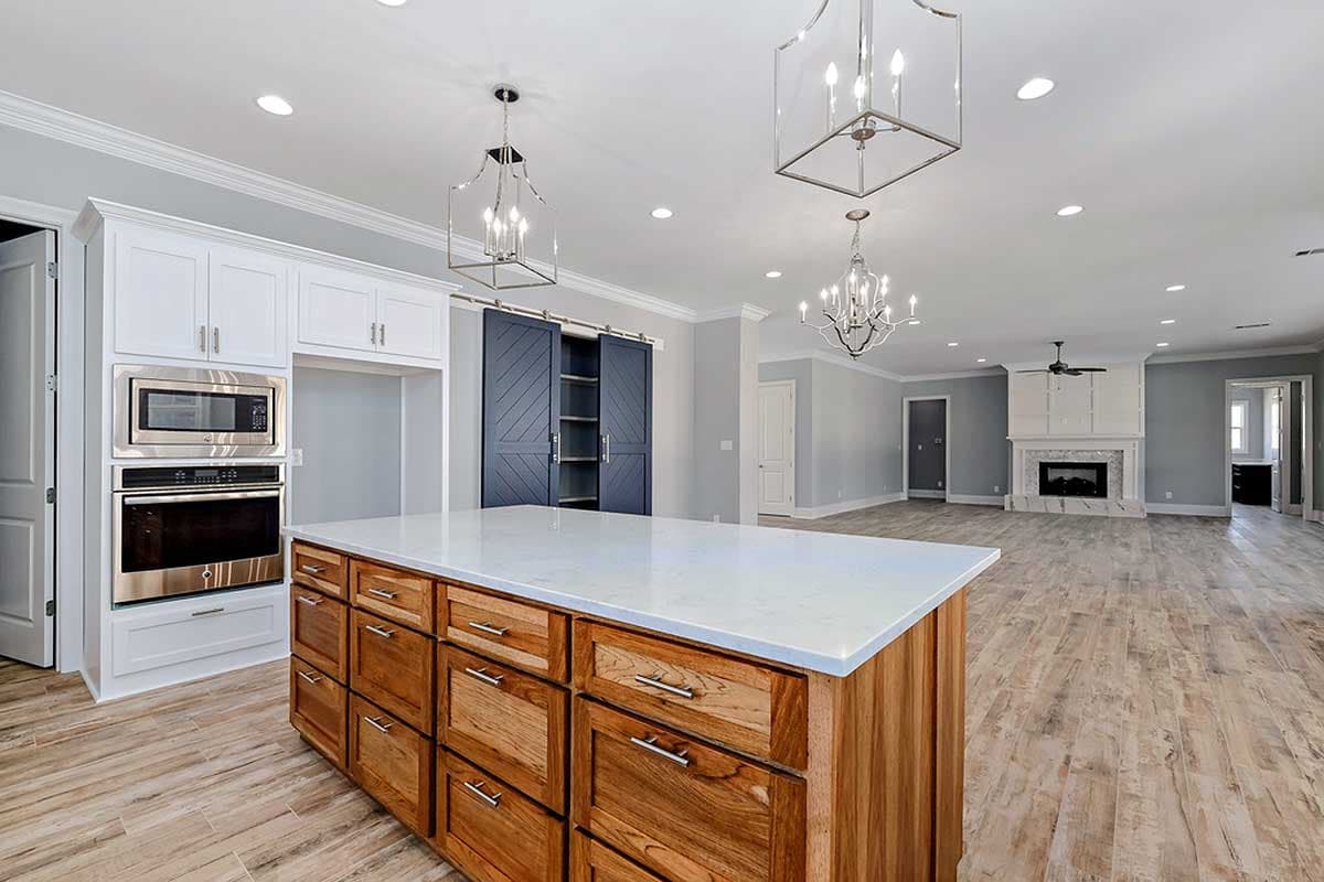 Modern kitchen with wood island, white cabinets, built-in oven and microwave, and sliding barn doors. Open to living room with fireplace.
