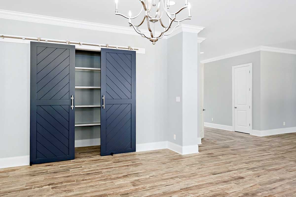 Interior view of a room with dark blue barn doors opening to shelves, light gray walls, crown molding, and wood-look flooring.
