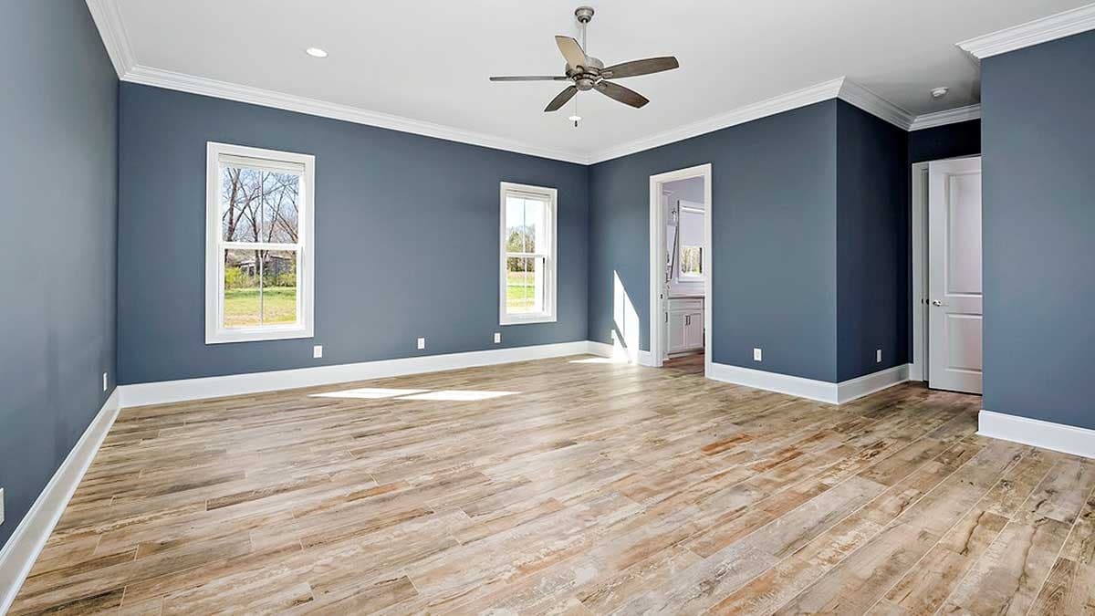 Interior view of a bedroom with two windows, wood-look flooring, ceiling fan, and doorway to an en-suite bathroom.