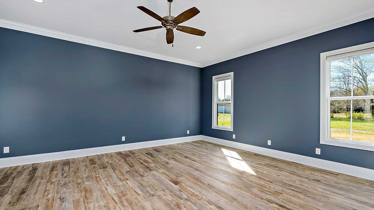 Interior view of an empty room with dark blue walls, wood-look flooring, a ceiling fan, recessed lighting, and two windows.