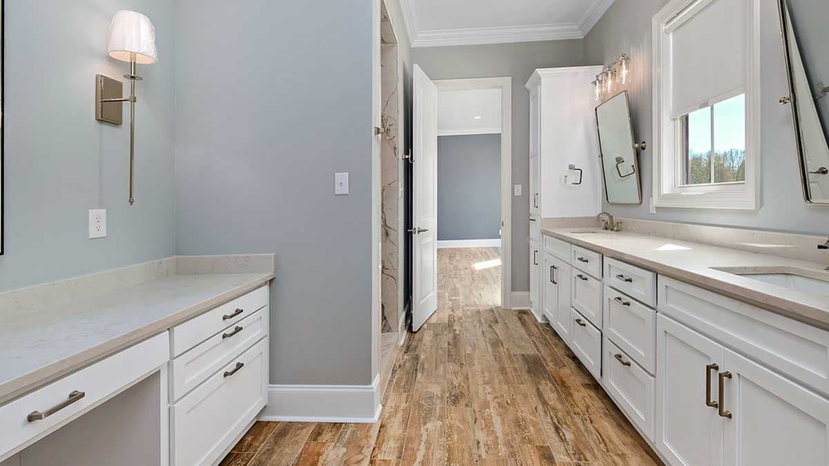 Double vanity with white cabinets and quartz countertops in a bathroom with wood-look flooring and a doorway to another room.