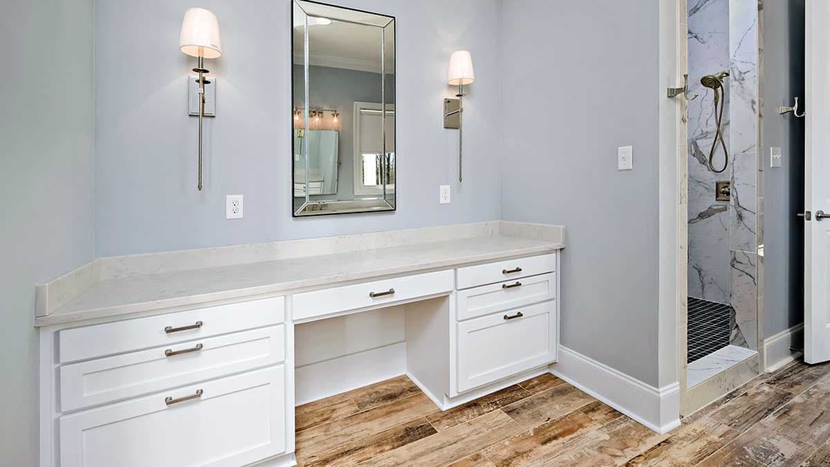 Bathroom vanity with white cabinetry, quartz countertop, and adjacent tiled shower with brass fixtures.