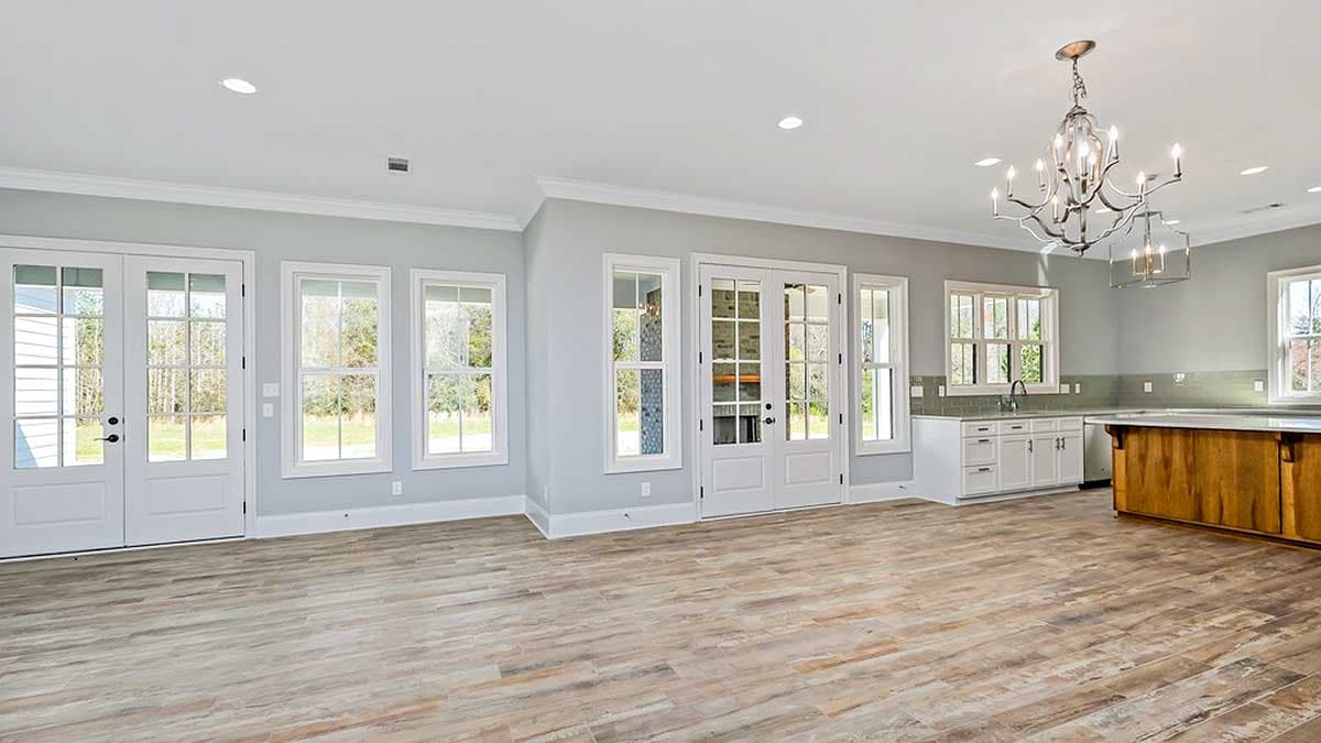 Interior view of a great room with double doors, multiple windows, a kitchen island, and white cabinetry.