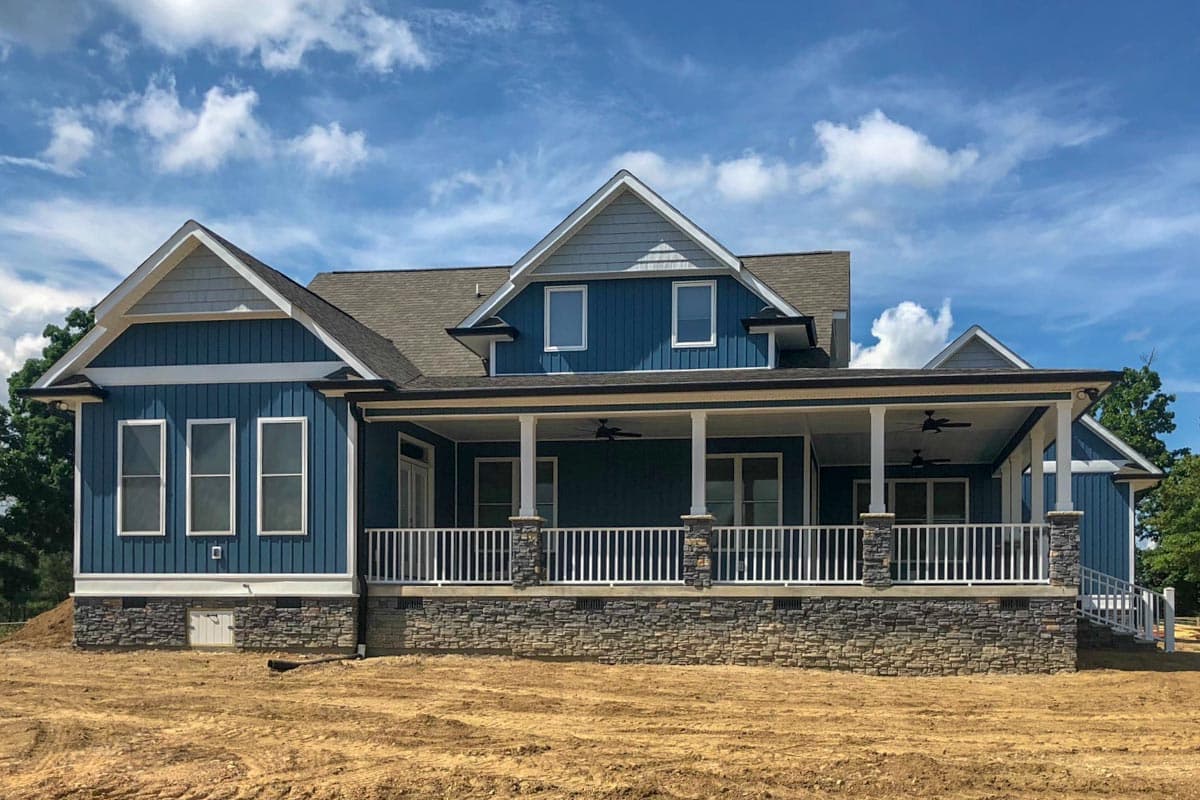House plan exterior: Modern Farmhouse style, two stories, with a deep wraparound porch supported by stone-clad columns and white railings.
