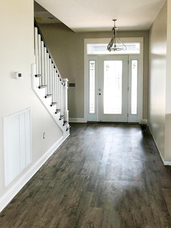 Interior view of home entryway with stairs, white banister, dark wood flooring, and glass-paneled double doors with sidelights.