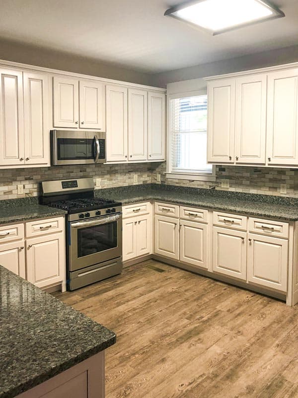 Kitchen with white cabinets, granite countertops, stainless steel appliances, and wood-look flooring.