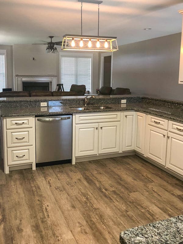 Kitchen interior with white cabinets, granite countertops, stainless steel dishwasher, and fireplace visible in background.