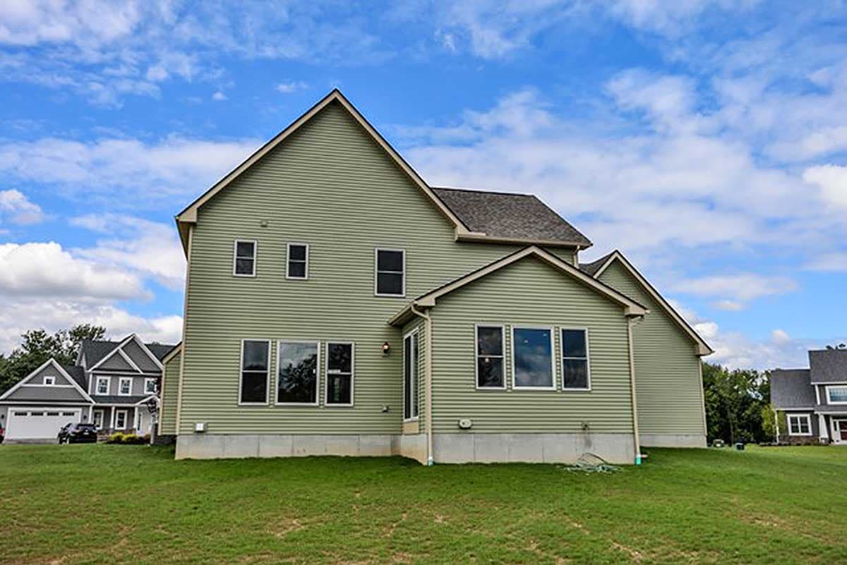 Two-story house plan exterior with green siding, prominent gables, multiple windows, and a side-facing garage visible in the background.