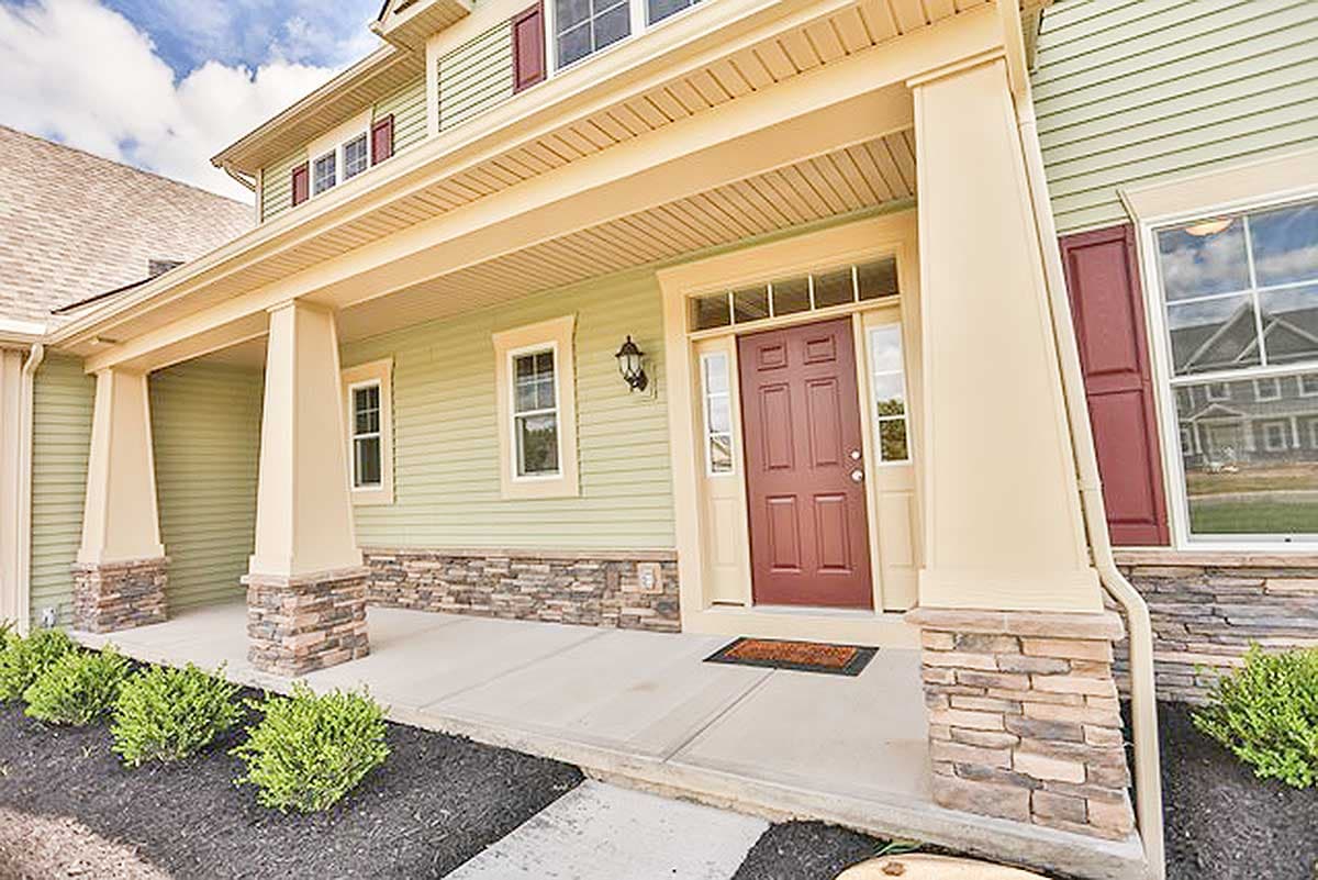 House plan exterior with a covered porch, stone accents, gable rooflines, and dormer windows.