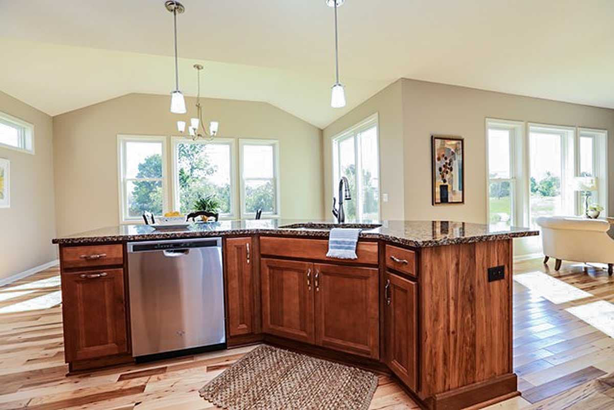 Kitchen island with granite countertop, sink, and dishwasher, featuring vaulted ceiling and large windows.