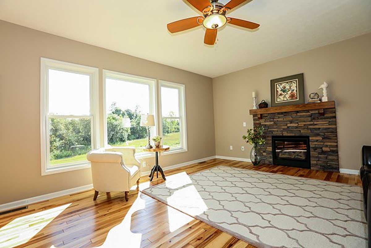 Interior view of a living room with a stone fireplace, large windows, and a ceiling fan.