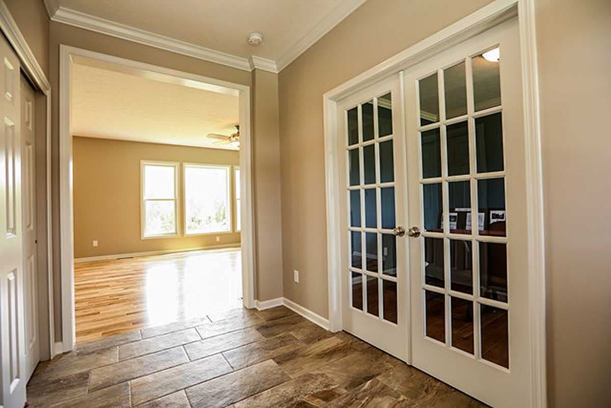 Interior view of an entryway with French doors leading to a room with large windows and hardwood floors.