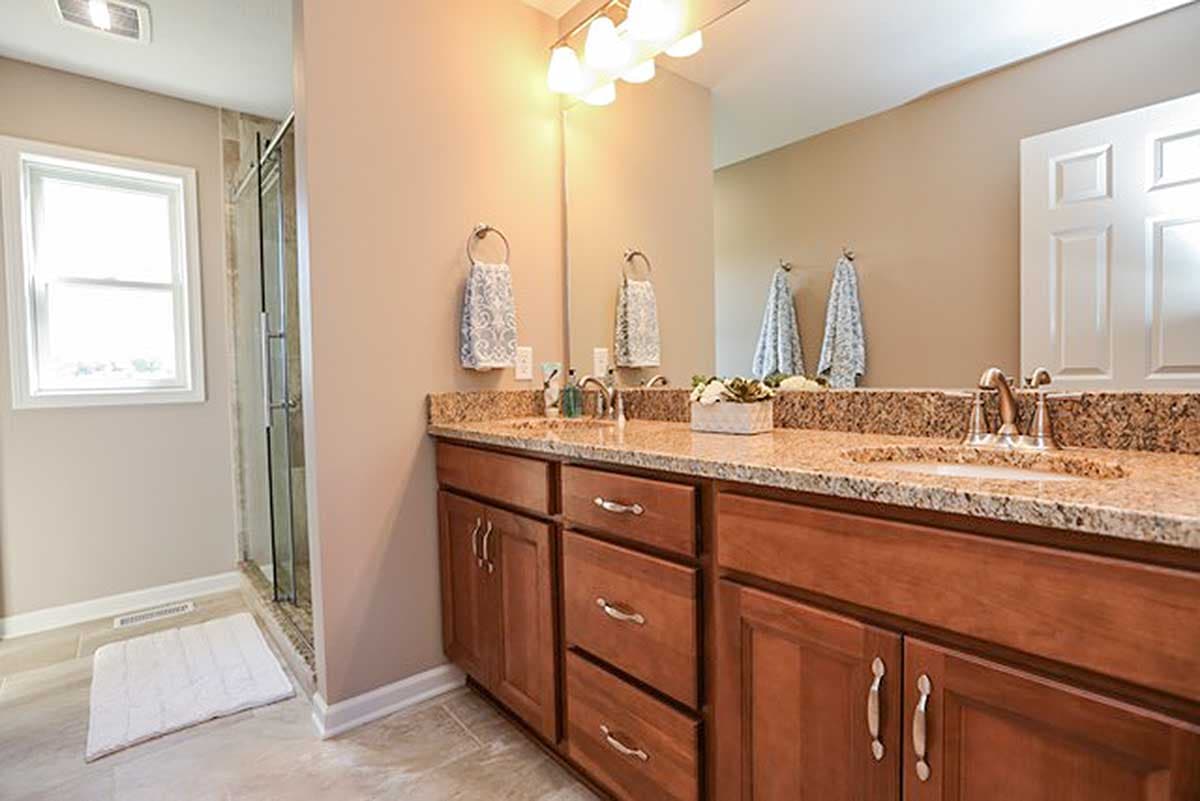 Bathroom with dual vanities, granite countertops, wood cabinets, and glass-enclosed shower.