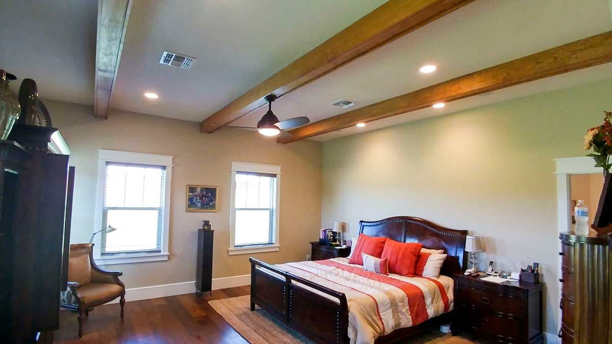 Bedroom interior with exposed wooden ceiling beams, a ceiling fan, recessed lighting, and two windows.