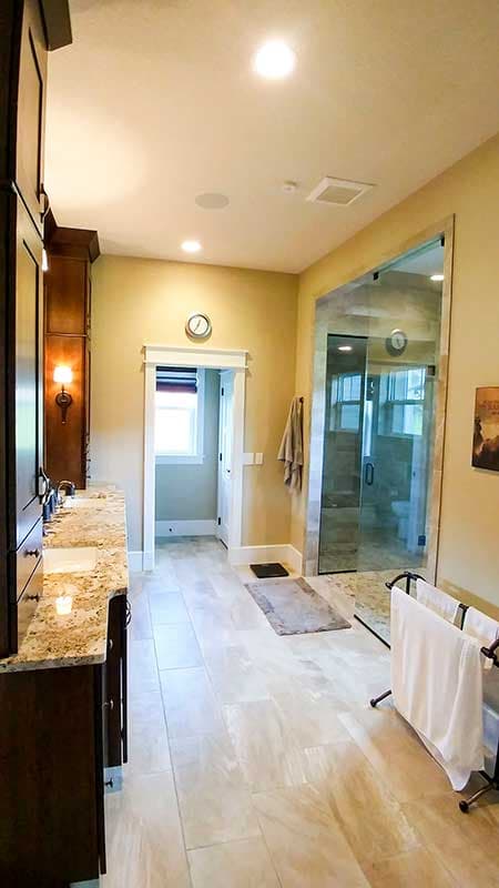 Bathroom with double vanity, large tiled shower with glass door, and natural light from window.