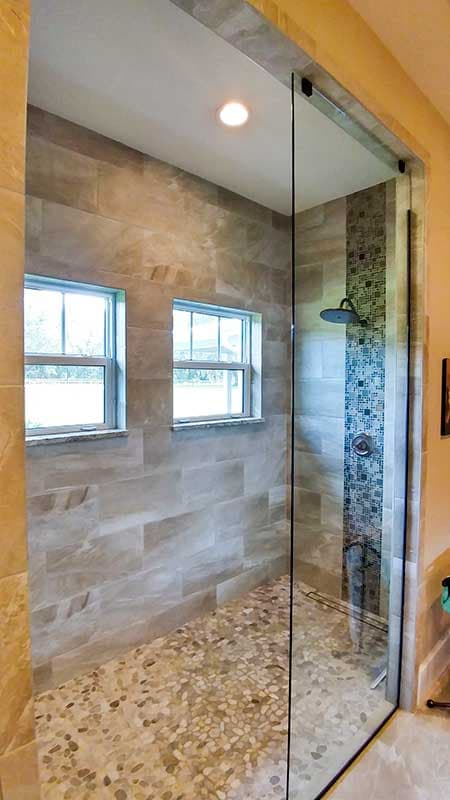 Tiled walk-in shower with two windows, a pebble floor, and a glass door.