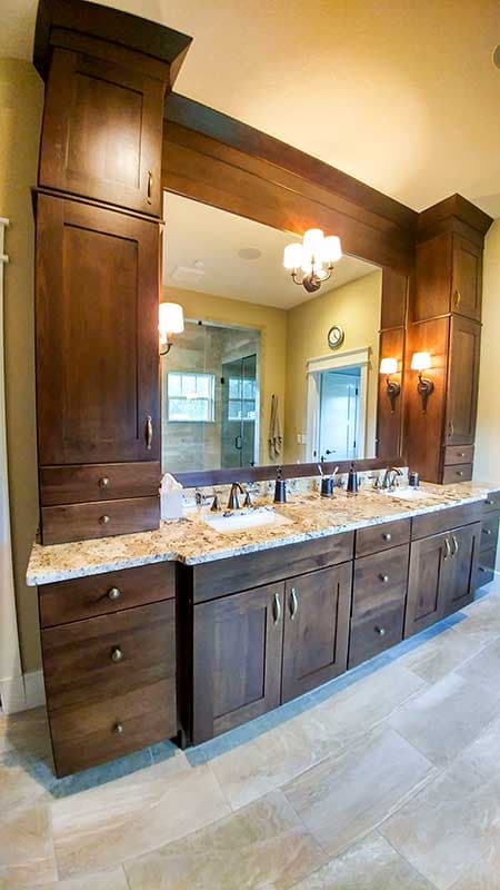 Bathroom vanity with dark wood cabinetry, granite countertops, dual sinks, and a large mirror reflecting a glass shower.