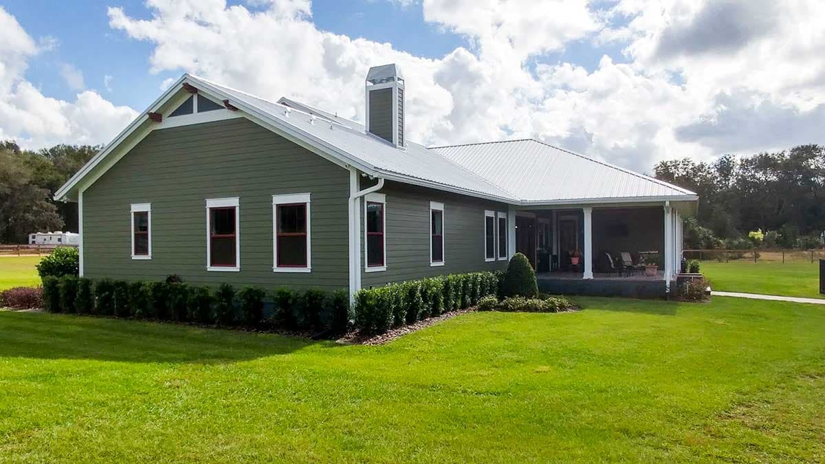 House plan exterior: Ranch style, green siding, metal roof, prominent chimney, and covered porch with columns.