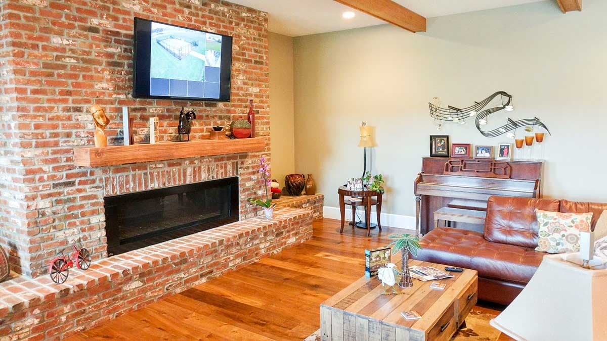 Living room with brick fireplace, wood floors, leather couch, piano, and coffee table.