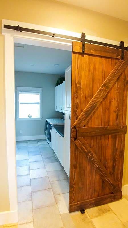 Laundry room with white cabinets, washer and dryer, visible through an open doorway with a wooden barn door.