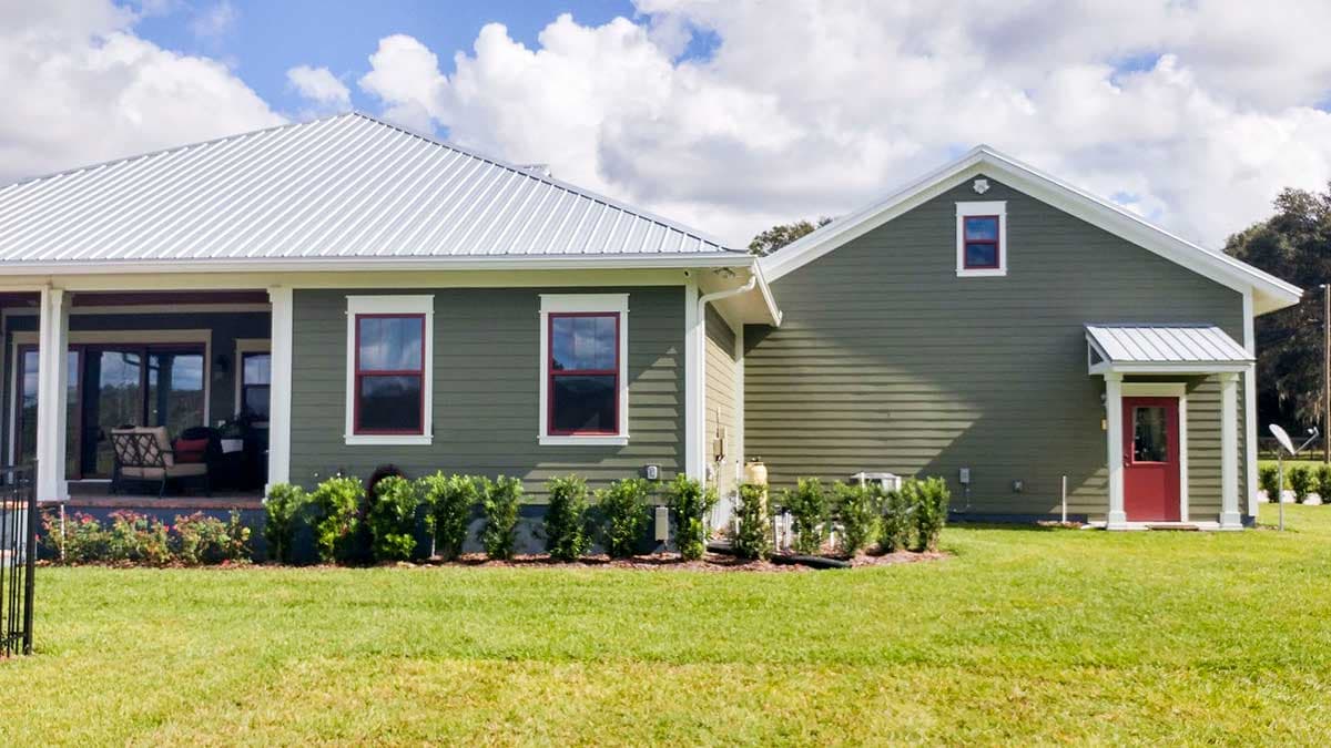 House plan exterior: Single-story modern farmhouse with metal roof, covered porch, and red front door with metal awning.