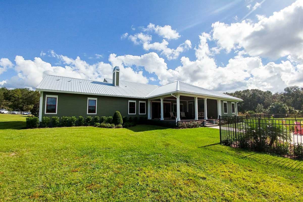 House plan exterior: one-story home with a wraparound porch, metal roof, and prominent chimney.