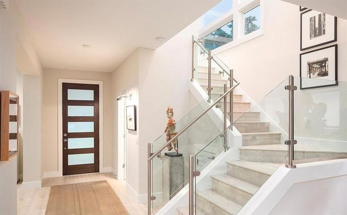Interior view of entryway with modern wood door with glass panes and floating staircase with glass railings.