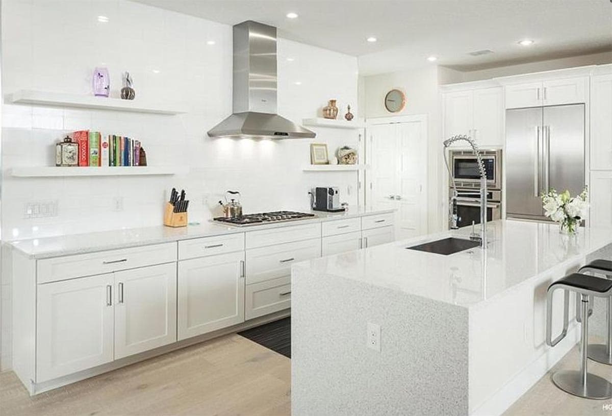 Modern white kitchen with island, stainless steel appliances, gas range, and waterfall countertop.