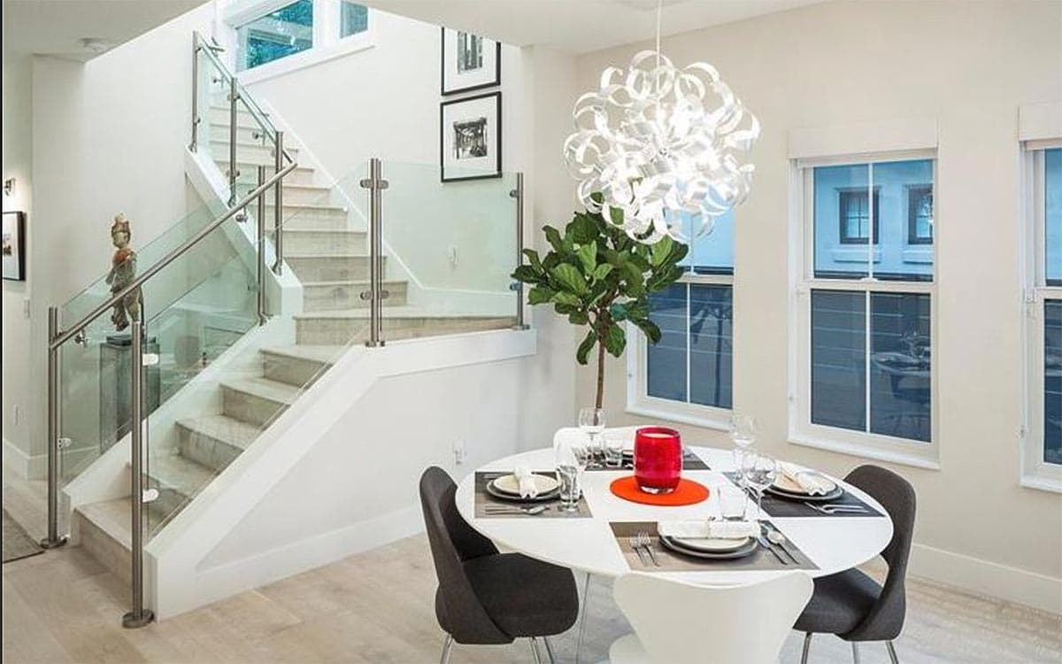 Interior view of dining area and modern staircase with glass railing. Dining table set for four.