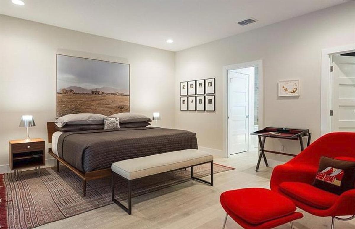 Bedroom with king-size bed, artwork, gallery wall, contemporary desk, and red accent chair.