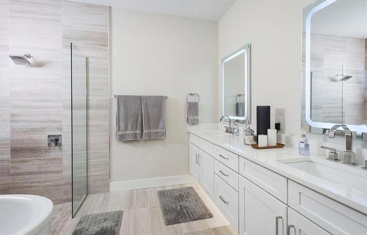 Modern bathroom with a dual vanity, glass-enclosed shower with stone tile, and LED-lit mirrors.