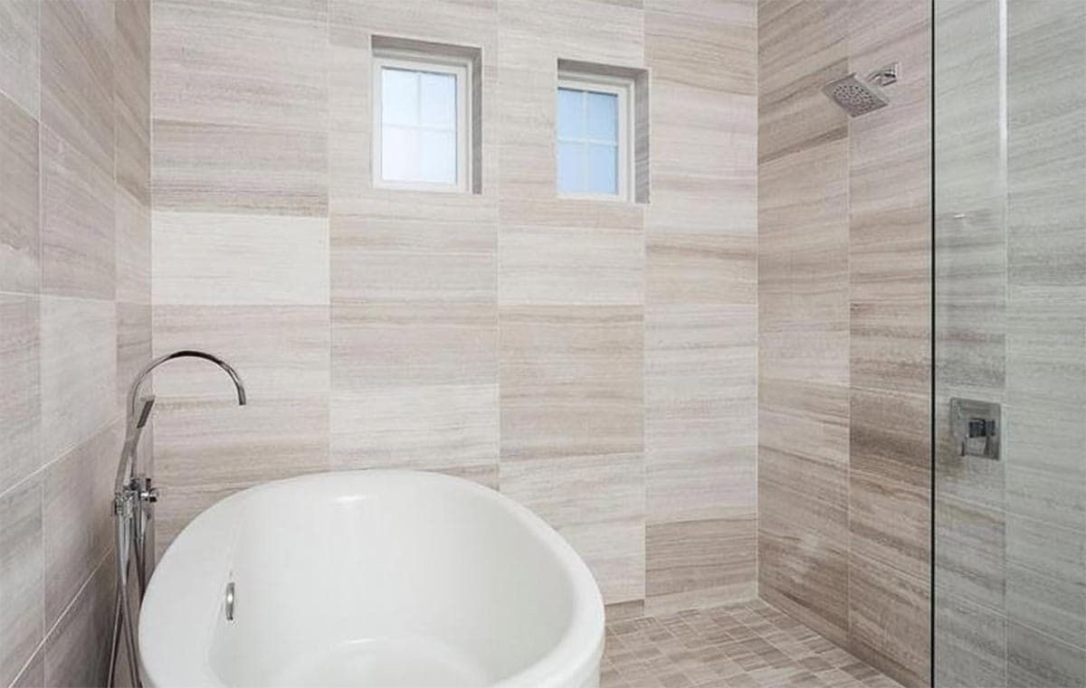 Freestanding tub and walk-in shower with wood-look tile walls and dual windows above tub.