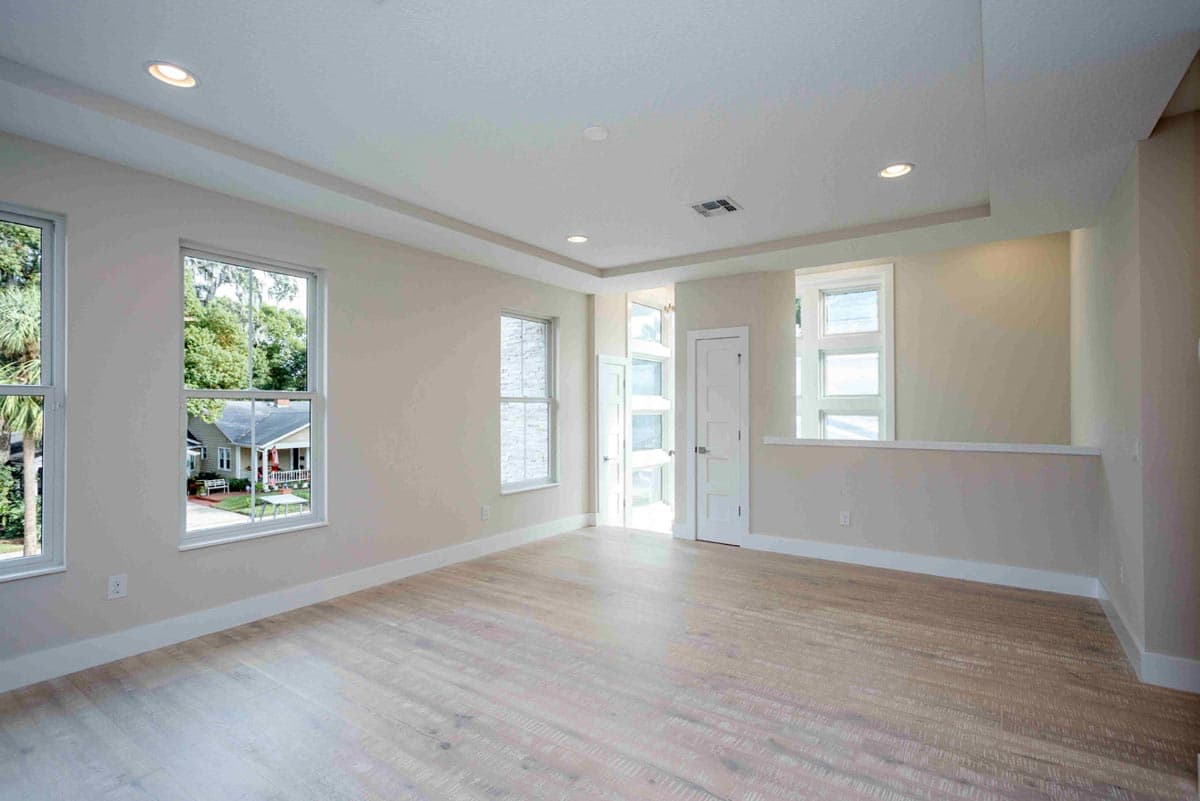 Interior view of an empty room with a tray ceiling, recessed lighting, multiple windows, and a door leading to a bright area.
