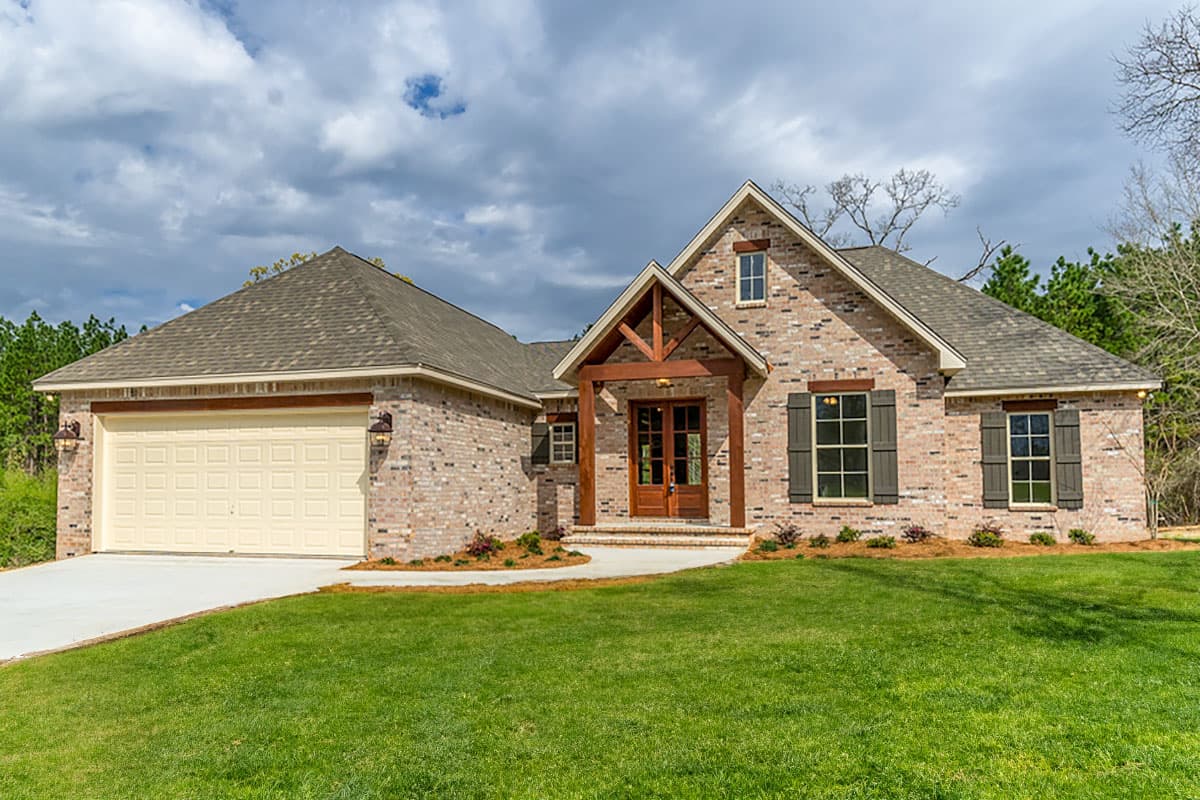 House plan exterior. One-story brick home with gabled roof, timber-framed entry porch, and attached garage. Includes shutters and dormer.