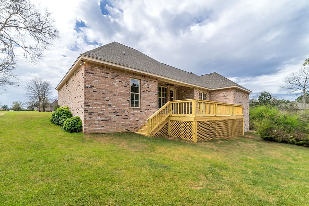 House plan exterior of a two-story brick home with a large wooden deck and lattice skirt.