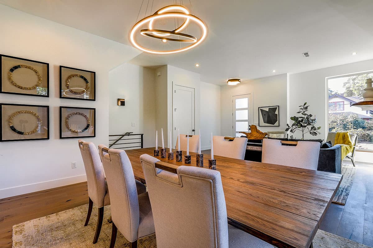 Dining room with wooden table, upholstered chairs, modern chandelier, and artwork on wall.
