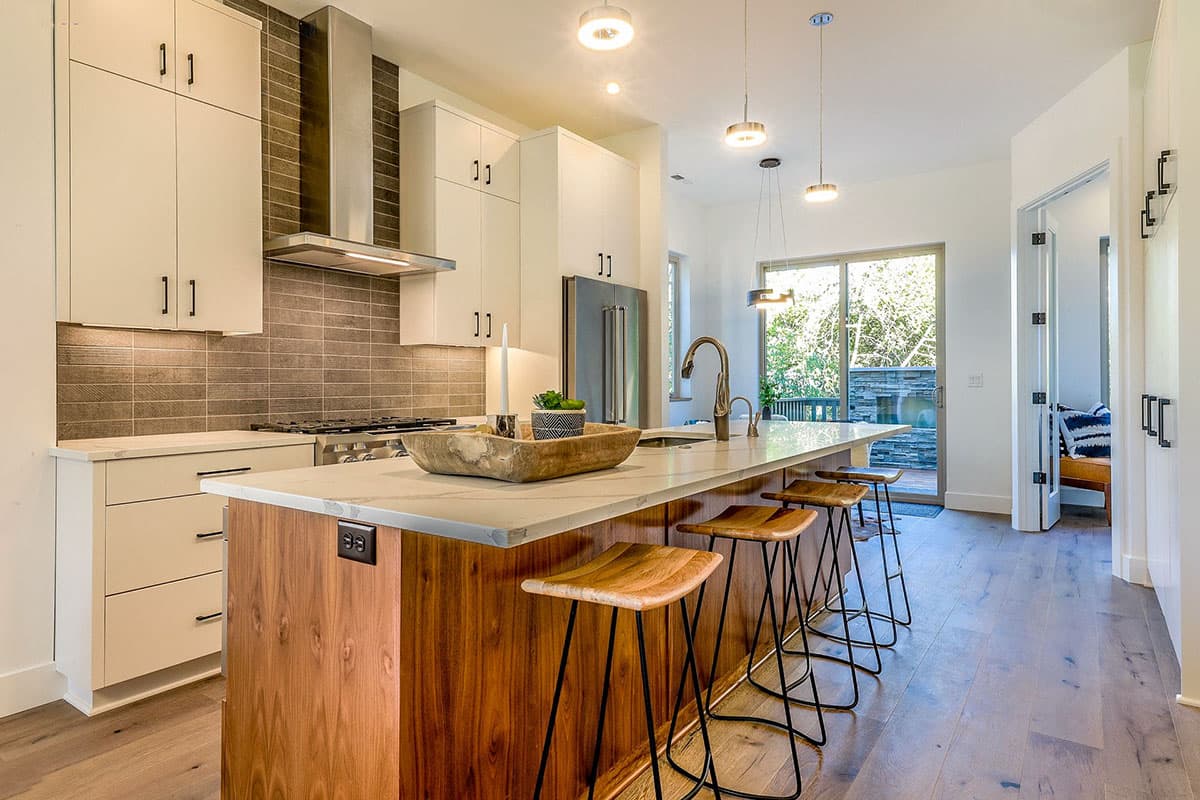 Contemporary kitchen with waterfall island, wood base cabinets, white uppers, stainless steel range hood, and pendant lighting.