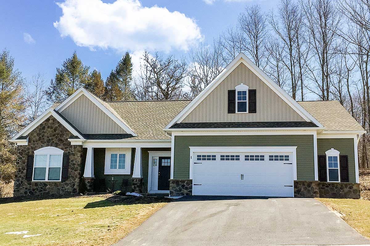 House plan exterior with stone accents, gabled rooflines, and a two-car garage. Features include decorative shutters and a covered porch area.